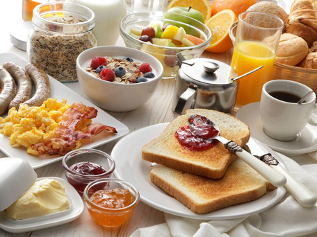 Frühstückstisch mit Toast, Marmelade, Müsli mit Beeren, Croissants, Orangensaft, Kaffee, Butter und weiteren Beilagen.